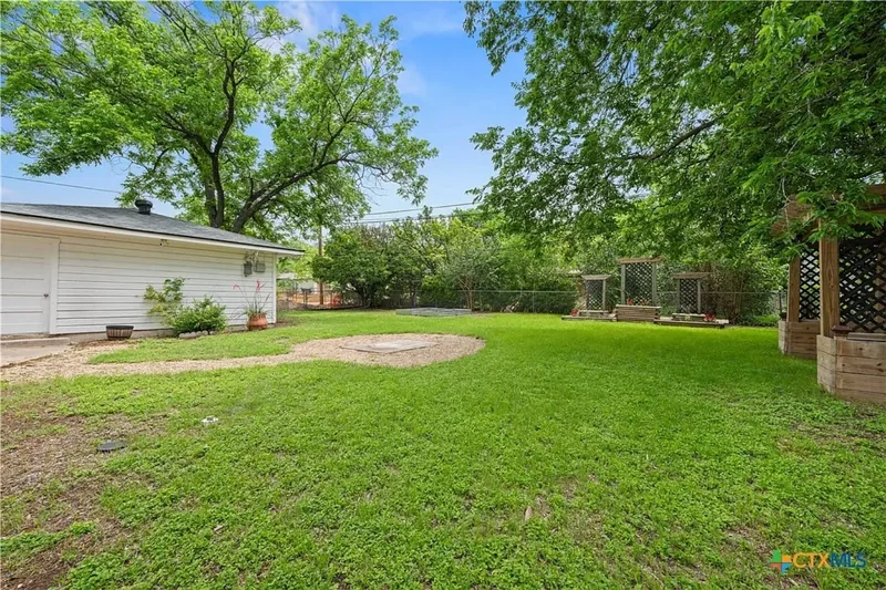 Large green backyard with mature trees, garage and garden structures